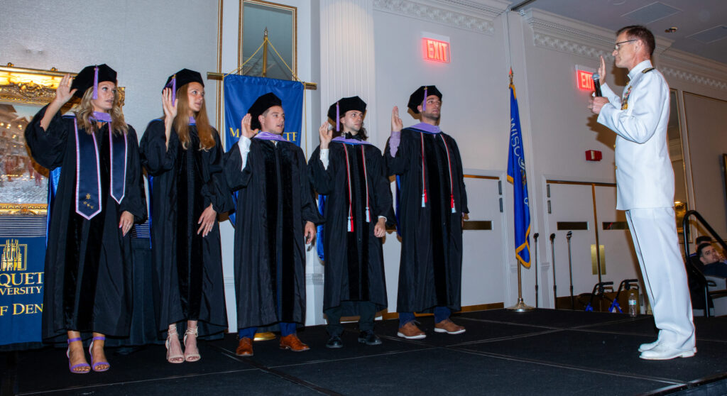 Five dental students in graduation robes raise their right hands.