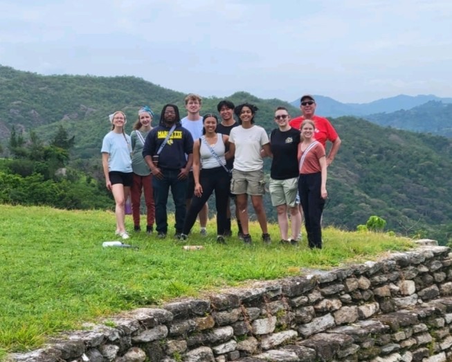 a group of students and faculty member pose in front of a jungle landscape.