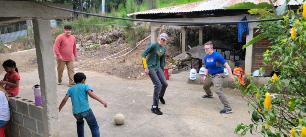 students and children from the community kick a soccer ball around.