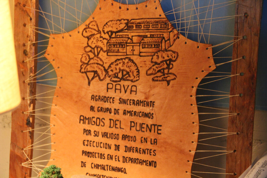 a leather stitched keepsake with a drawing of a school building and text reading, "pava agradece sinceramente al grupo de americanos amigos del puente por su valioso apoyo en la ejecucion de diferentes proyectos en el departmento de chimaltenango..."