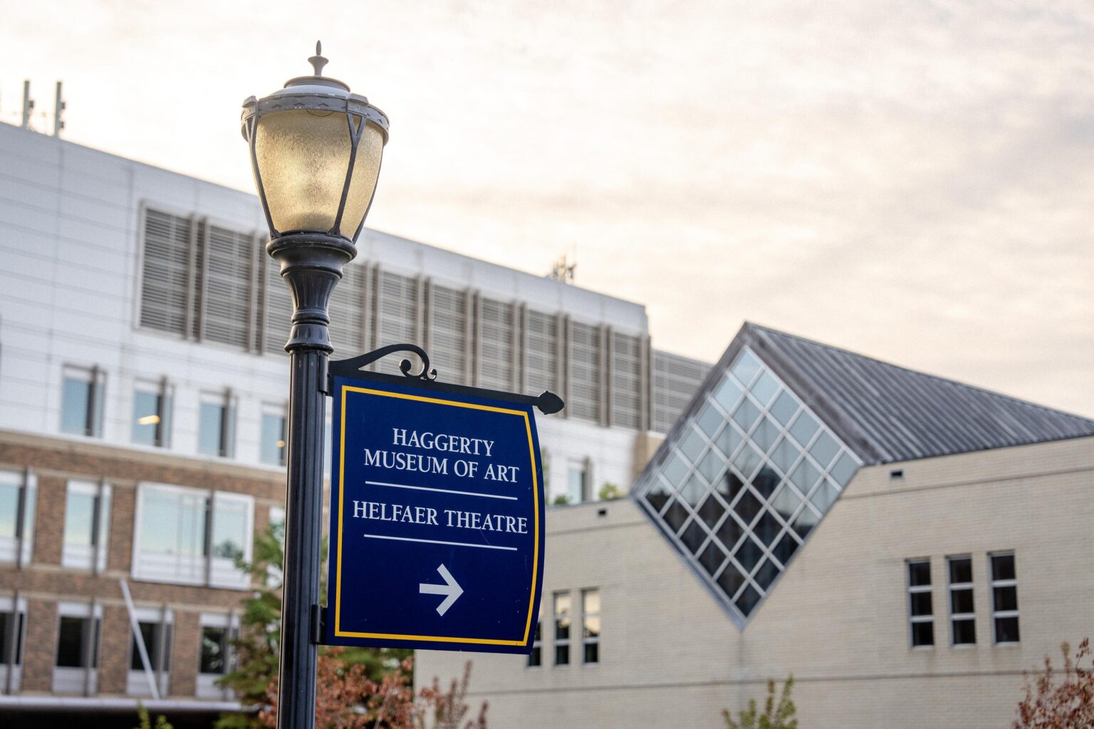 A blue sign pointing to the Haggerty Museum of Art with the museum in the background.