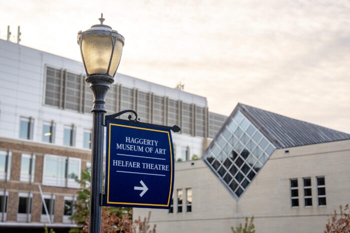 A blue sign pointing to the Haggerty Museum of Art with the museum in the background.
