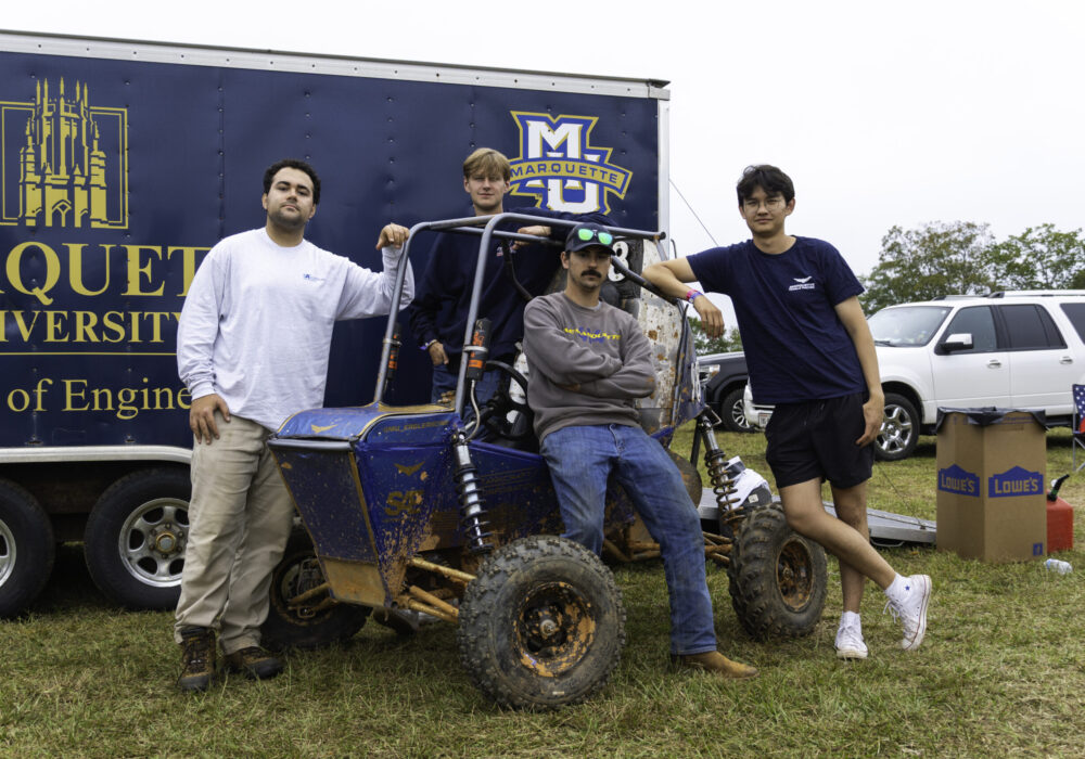 students posing with off-road racing vehicle in front of Marquette trailer