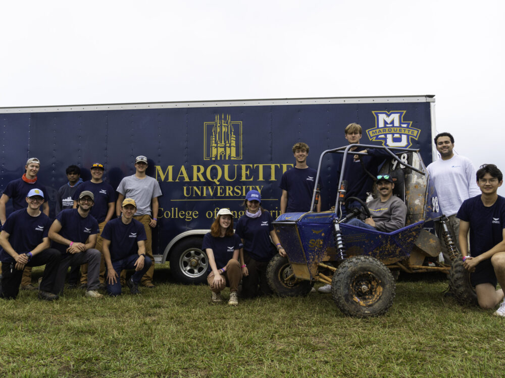 students posing with off-road racing vehicle in front of Marquette branded trailer