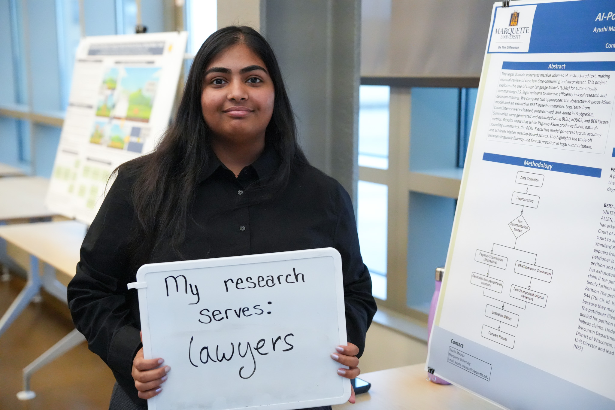 student holding a board that says "my research serves: lawyers" in front of a research poster