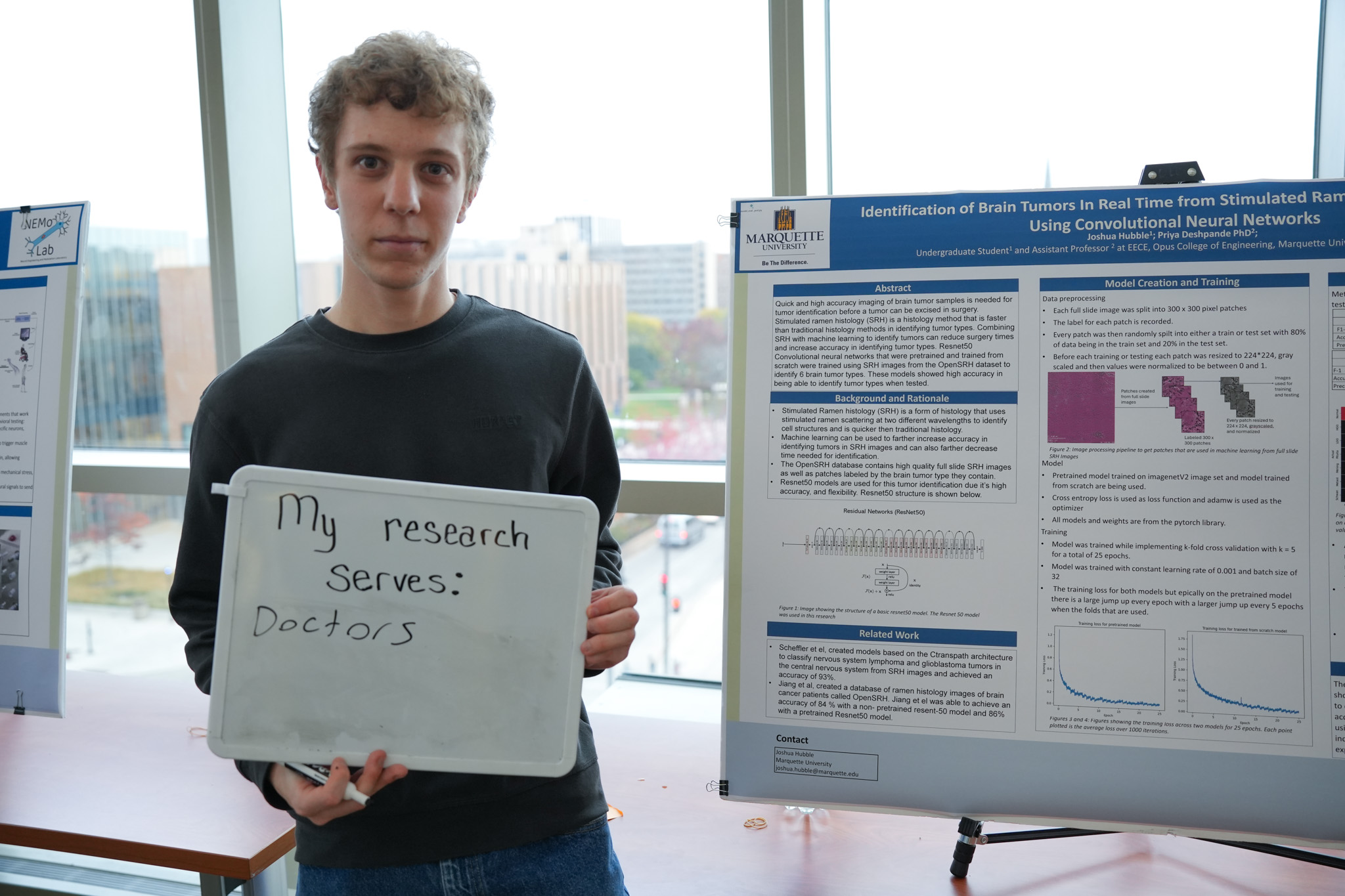 student holding a board that says "my research serves: doctors" in front of a research poster