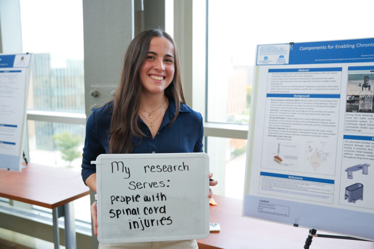 student holding a board that says "my research serves: people with spinal cord injuries" in front of a research poster