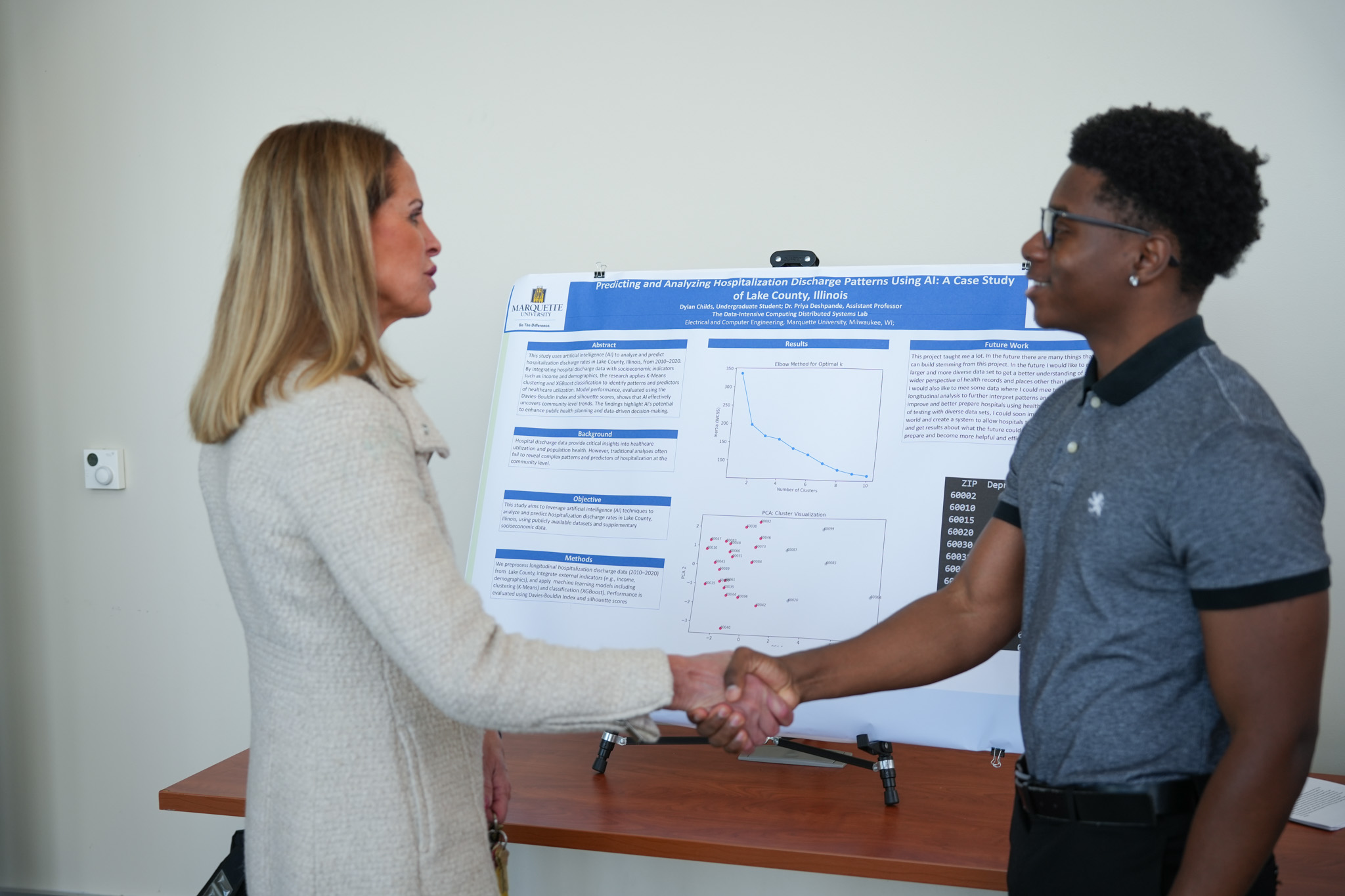 student and dean shaking hands in front of research poster