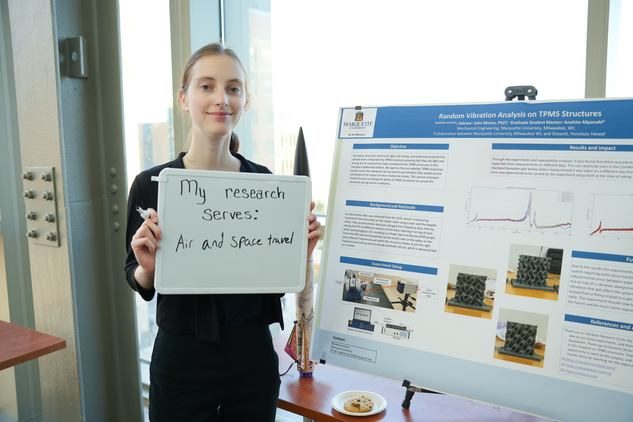 student holding a board that says "my research serves: air and space travel" in front of a research poster