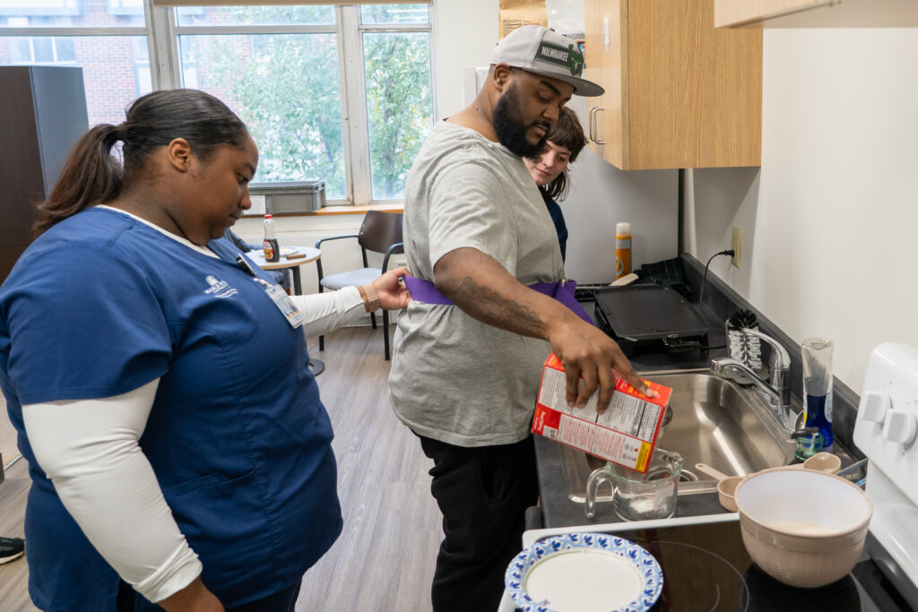 A student assisting a client making pancakes.