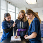 Two students assisting a patient write on a notepad.