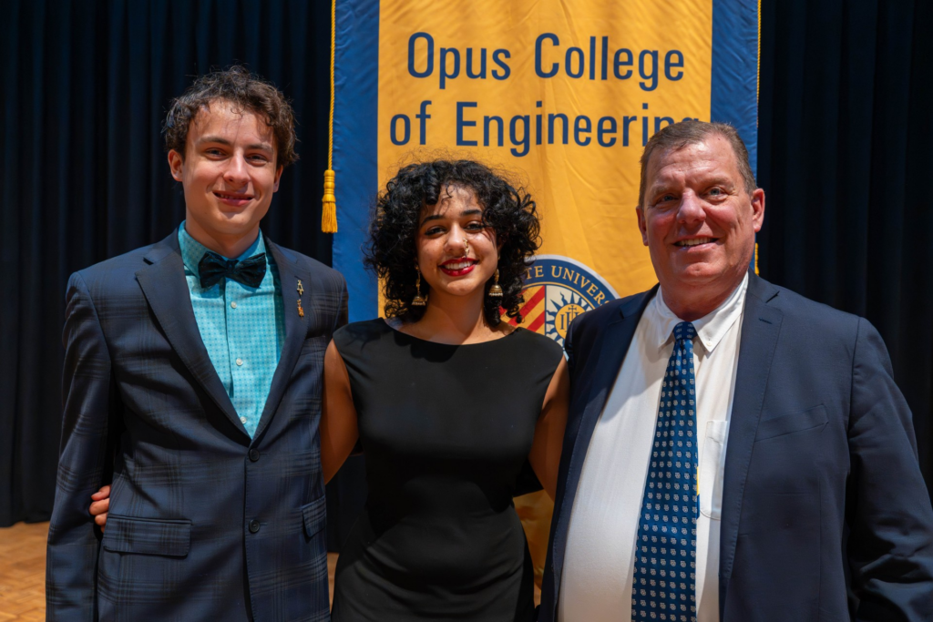 Two students posing with Dr. Marke Federle in front of Opus College banner at awards event