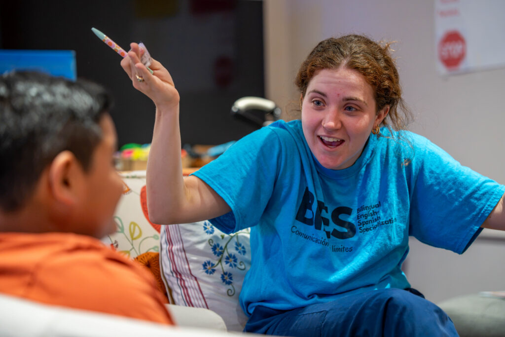 A student expressively talks with a client in Spanish while reading a book during therapy.