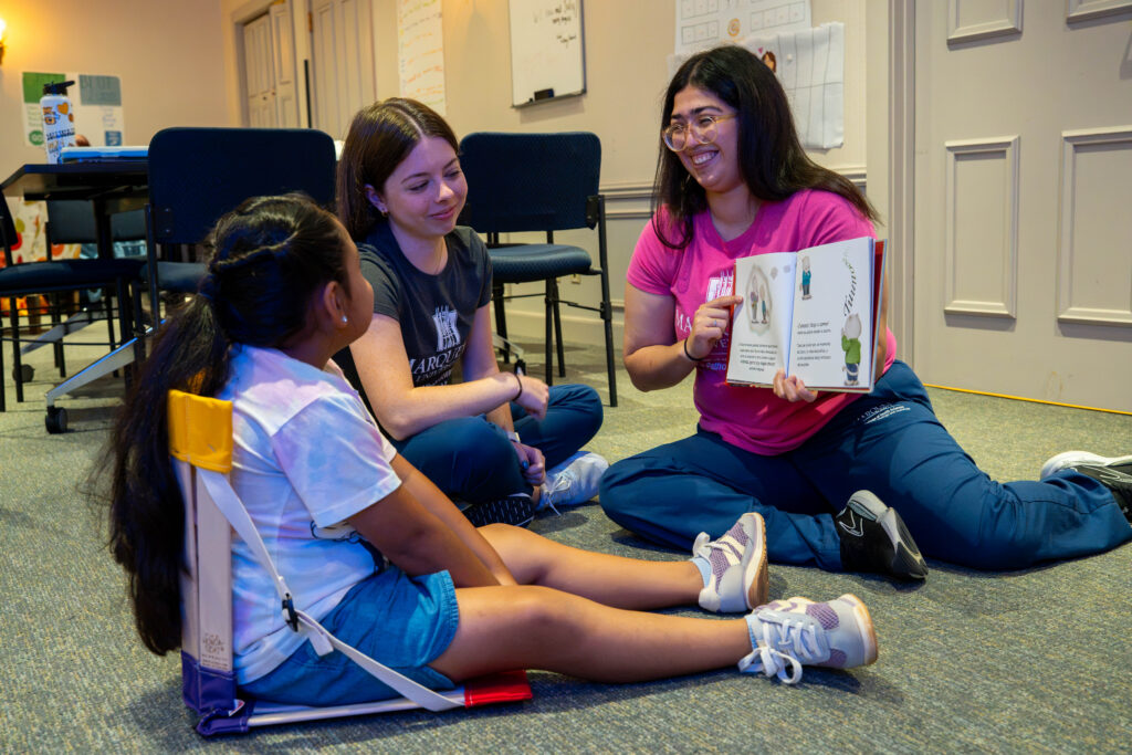 Two students sitting with a child reading a book.