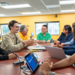 students and faculty collaborating around table and discussing their work