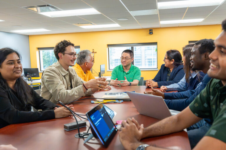 students and faculty collaborating around table and discussing their work